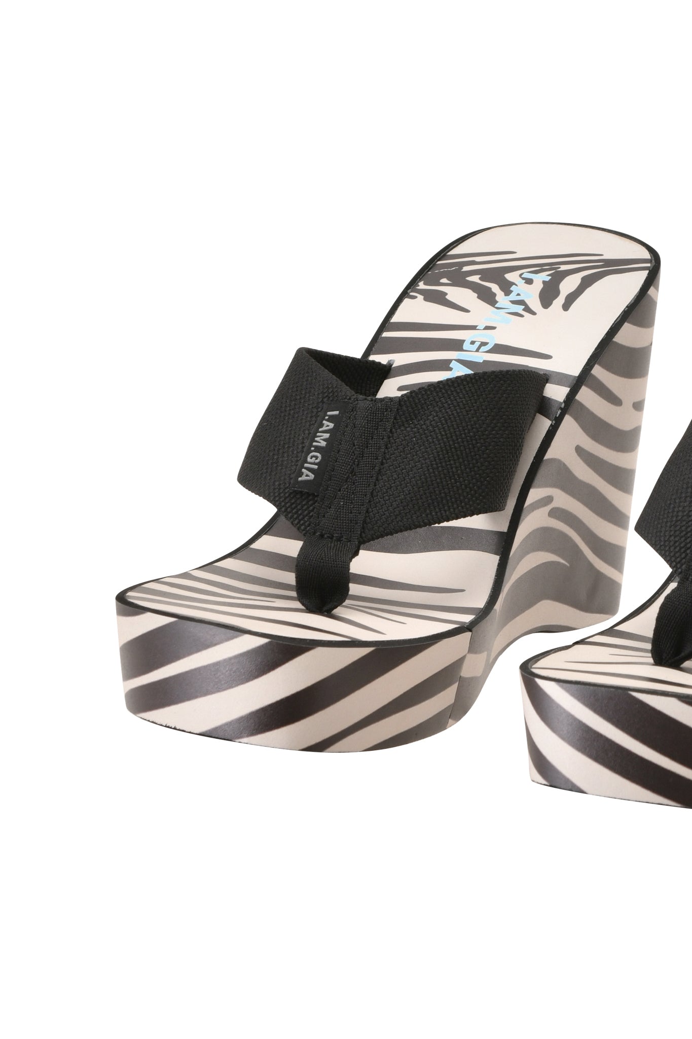 Elevate your style with the SHELBY FLIP FLOP - FINE LINE ZEBRA by I.AM.GIA, featuring bold black straps and a striking zebra print platform sole—these statement sandals are perfect for making an entrance. A glimpse of another matching sandal can be seen partially on the right side.