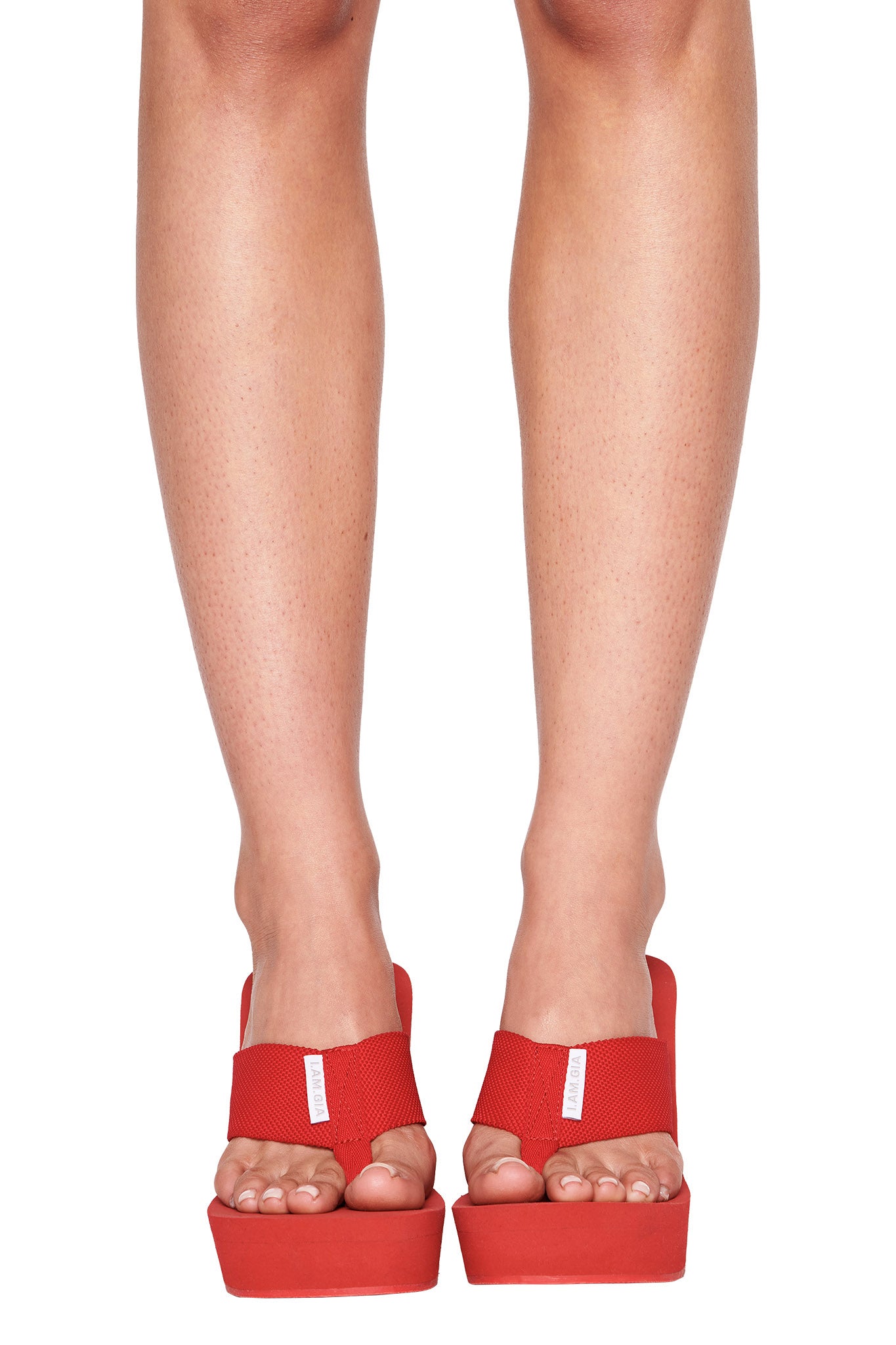 A pair of legs wearing the SHELBY FLIP FLOP in red from I.AM.GIA. The image, showcasing the red platform sandals with thick straps from the front, is focused on the feet and lower legs. The skin tone is light and the background is plain white.
