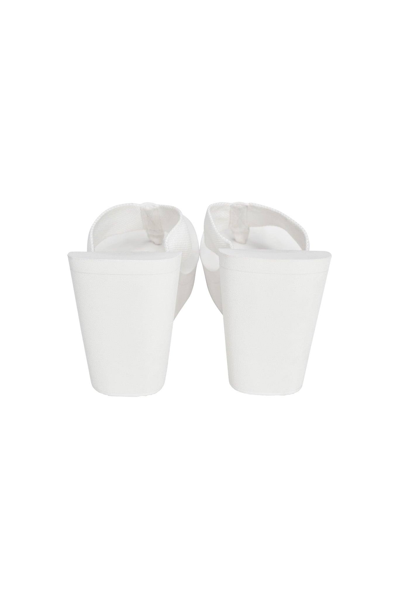 A pair of I.AM.GIA Shelby Flip Flops in white, viewed from the back. These sandals feature thick, high platform heels and a sleek strap design. The casual yet elevated style offers comfortable wear for any occasion due to the substantial height of the platform.