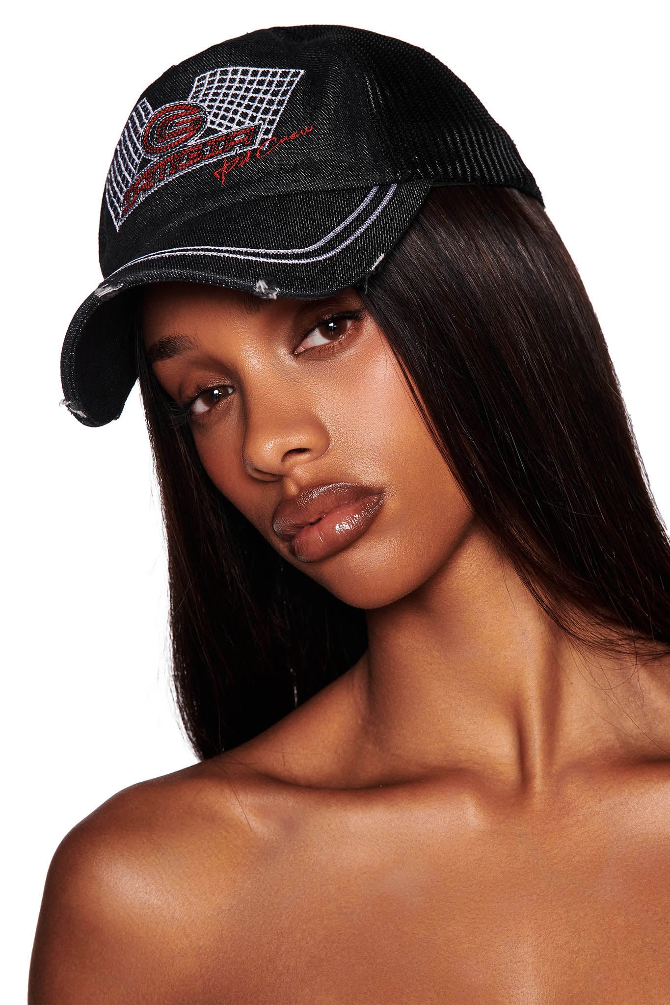 A person with long, straight hair is wearing the KIMANI CAP - BLACK from I.AM.GIA, featuring a red embroidered design and text on the front. The cap has a slightly worn look, and the person is posed against a plain white background.