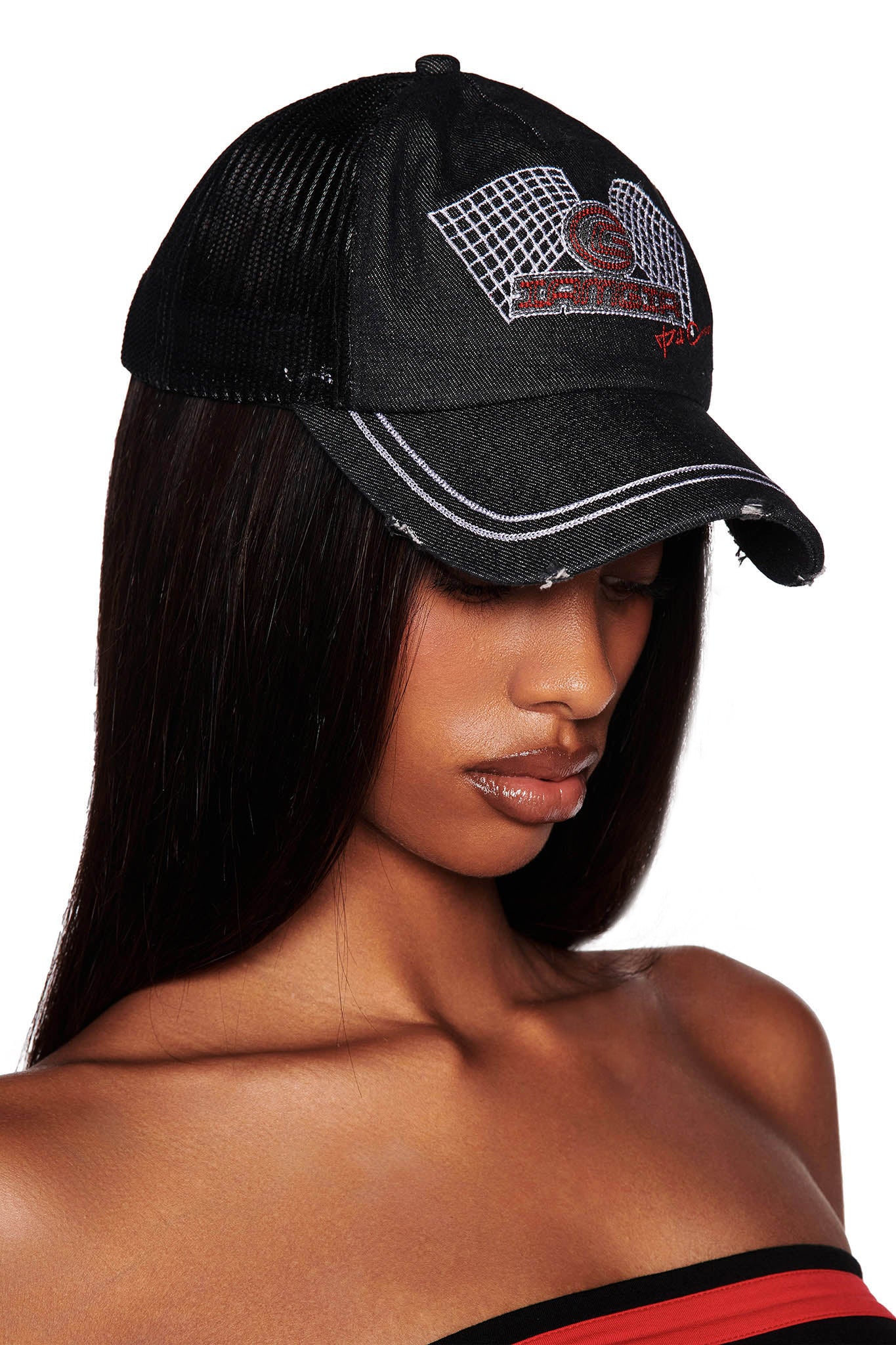 A person with long, straight hair is wearing the I.AM.GIA KIMANI CAP in black. The cap is adorned with a design of a basketball hoop and ball, as well as some text. The person is looking downward, and their shoulders are bare, suggesting they are wearing strapless clothing.
