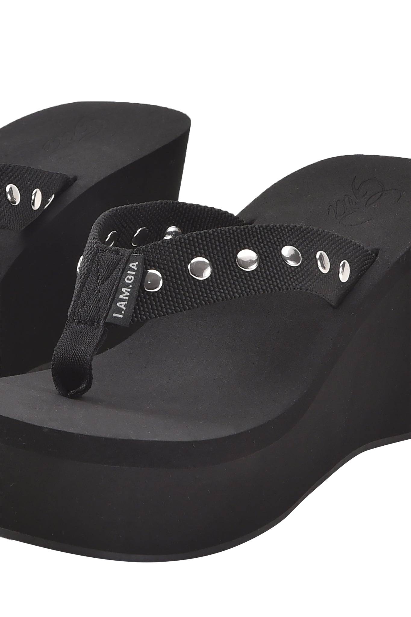 A close-up of the I.AM.GIA SHELBY STUDDED FLIP FLOP 2.0 in black, featuring thick platform soles, fabric straps with silver eyelets, and a small "SAMOA" tag for an edgy look.