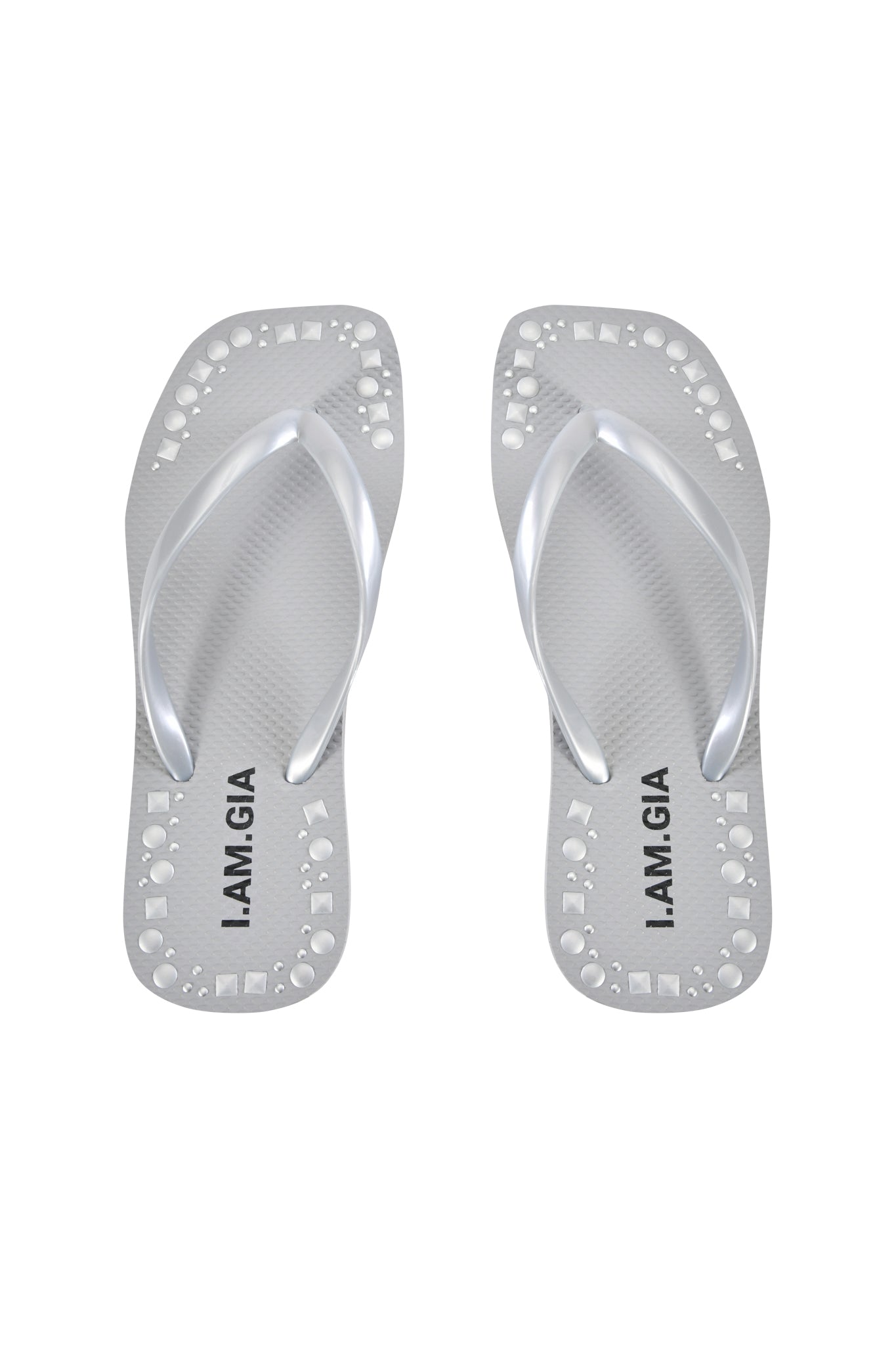 The INKA STUDDED FLIP FLOP - SILVER by I.AM.GIA features a comfortable footbed, textured soles, circular cutout designs along the edges, and the brand name in black on each footbed.