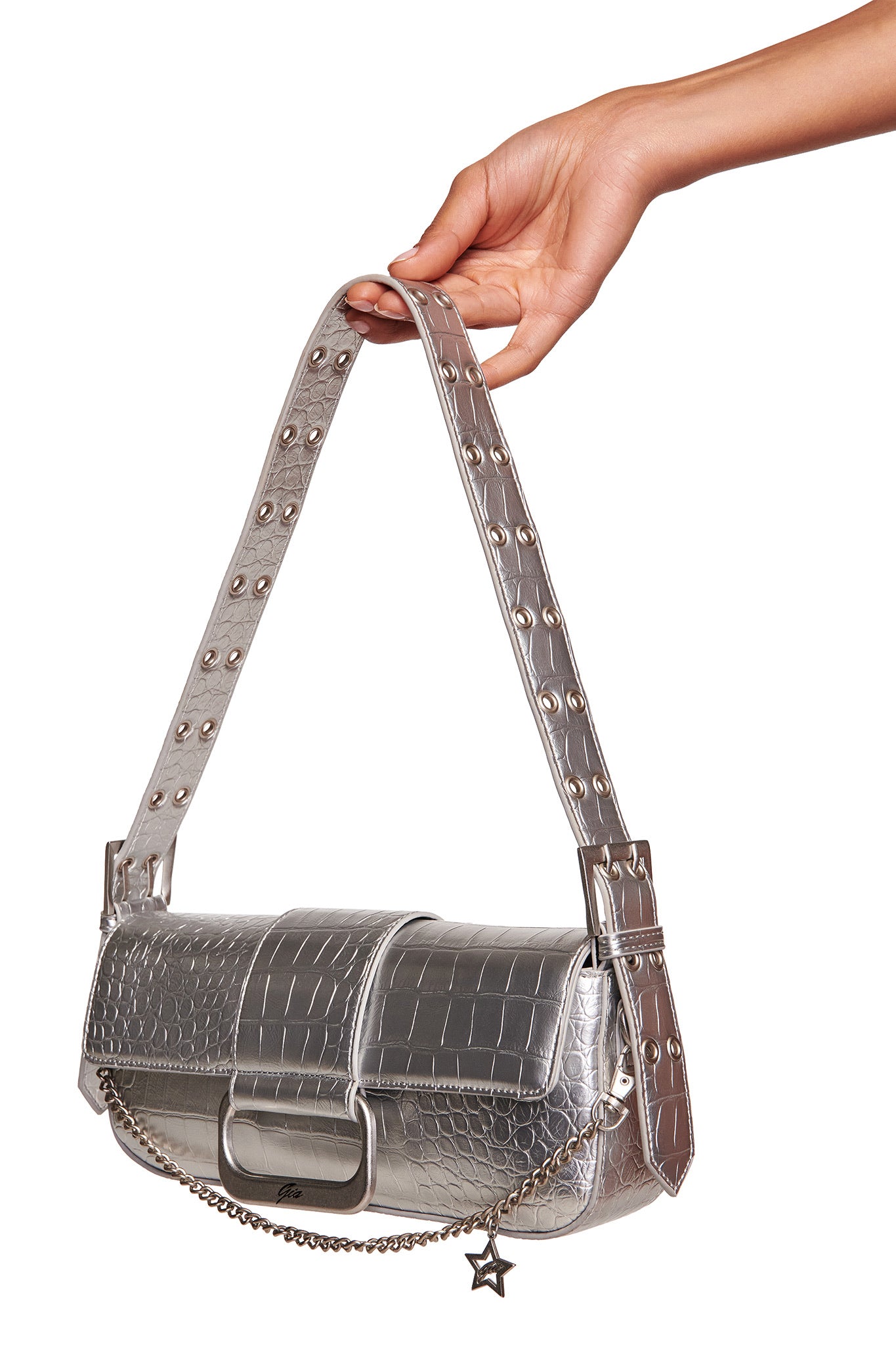 A hand holds the I.AM.GIA MILA METALLIC BAG in silver metallic, a mini shoulder purse with faux crocodile texture, studded strap, chain detail, star charm, and adjustable flap closure.