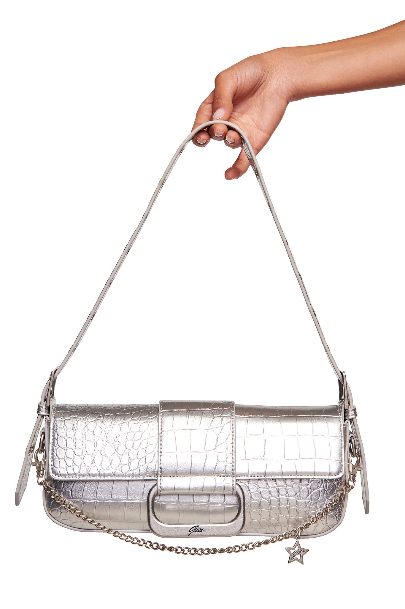 A hand holds the I.AM.GIA MILA METALLIC BAG in silver, showcasing a faux crocodile texture, adjustable strap, chain accent, and star-shaped charm.