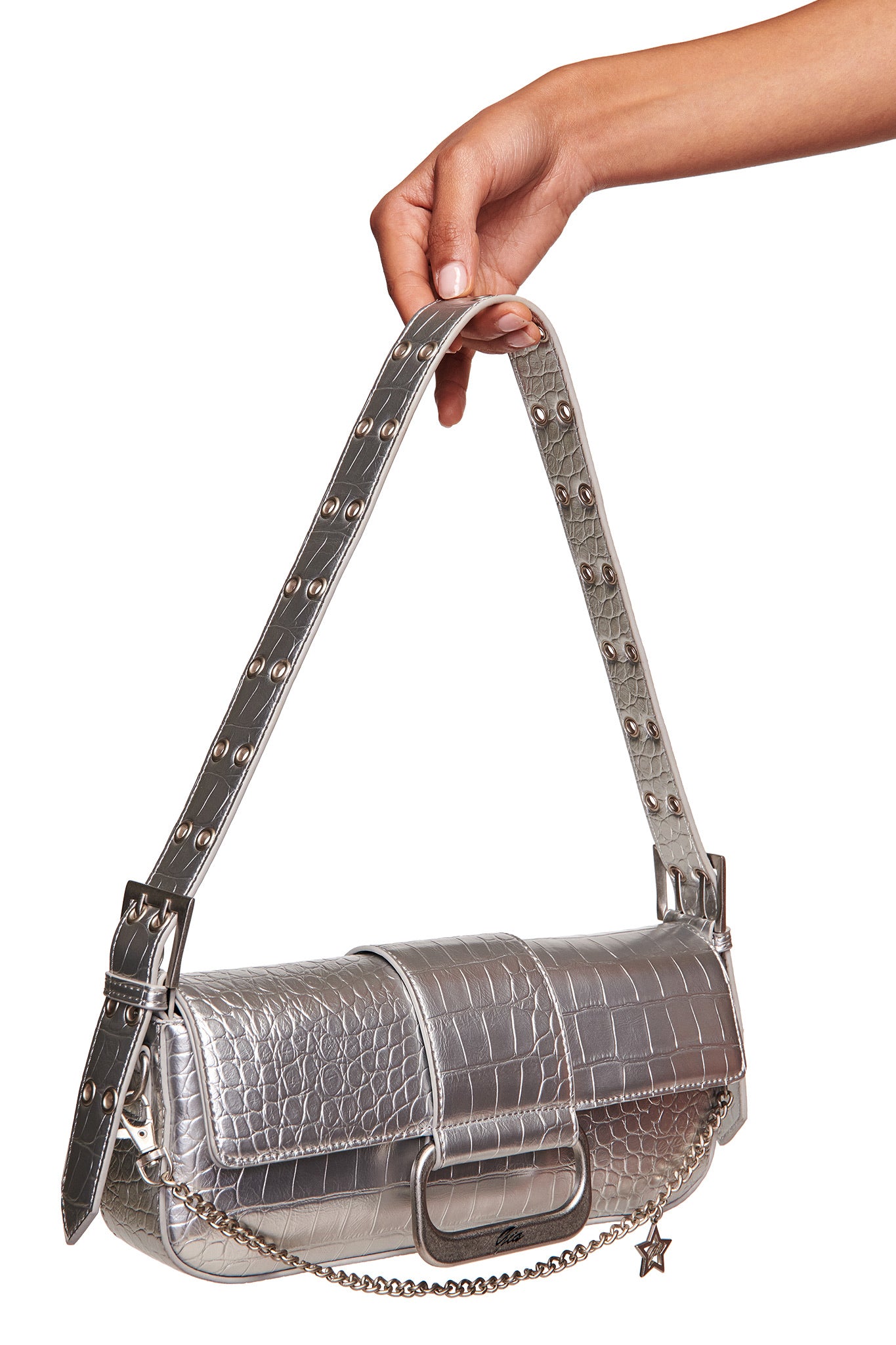 A hand holds the I.AM.GIA MILA METALLIC BAG in silver, a mini shoulder purse with faux crocodile texture, adjustable strap with metal eyelets, and a star charm hanging from a chain.