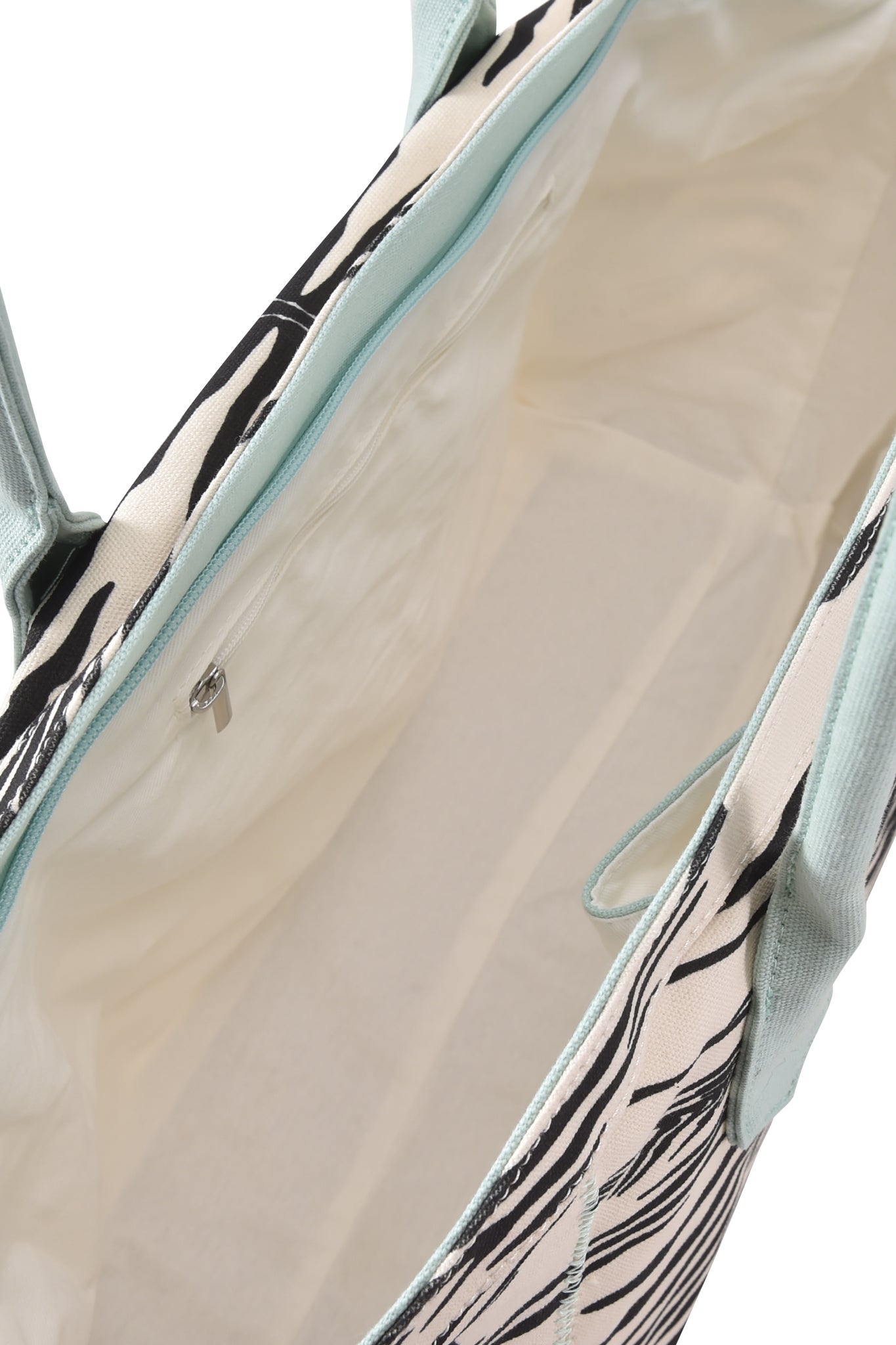 Open top view of the I.AM.GIA BLARE TOTE BAG - FINE LINE ZEBRA, featuring an oversized design with a light-colored interior, a zippered pocket, and mint green handles. The exterior showcases an abstract black and white zebra print.