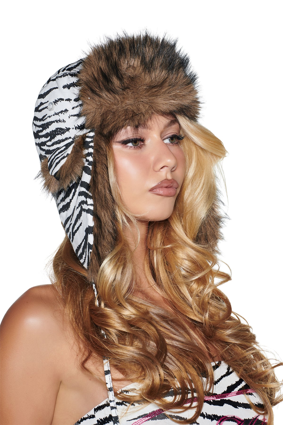A person wears an I.AM.GIA YVL FUR TRAPPER HAT - ZEBRA, featuring a black-and-white zebra print and brown faux fur trim.