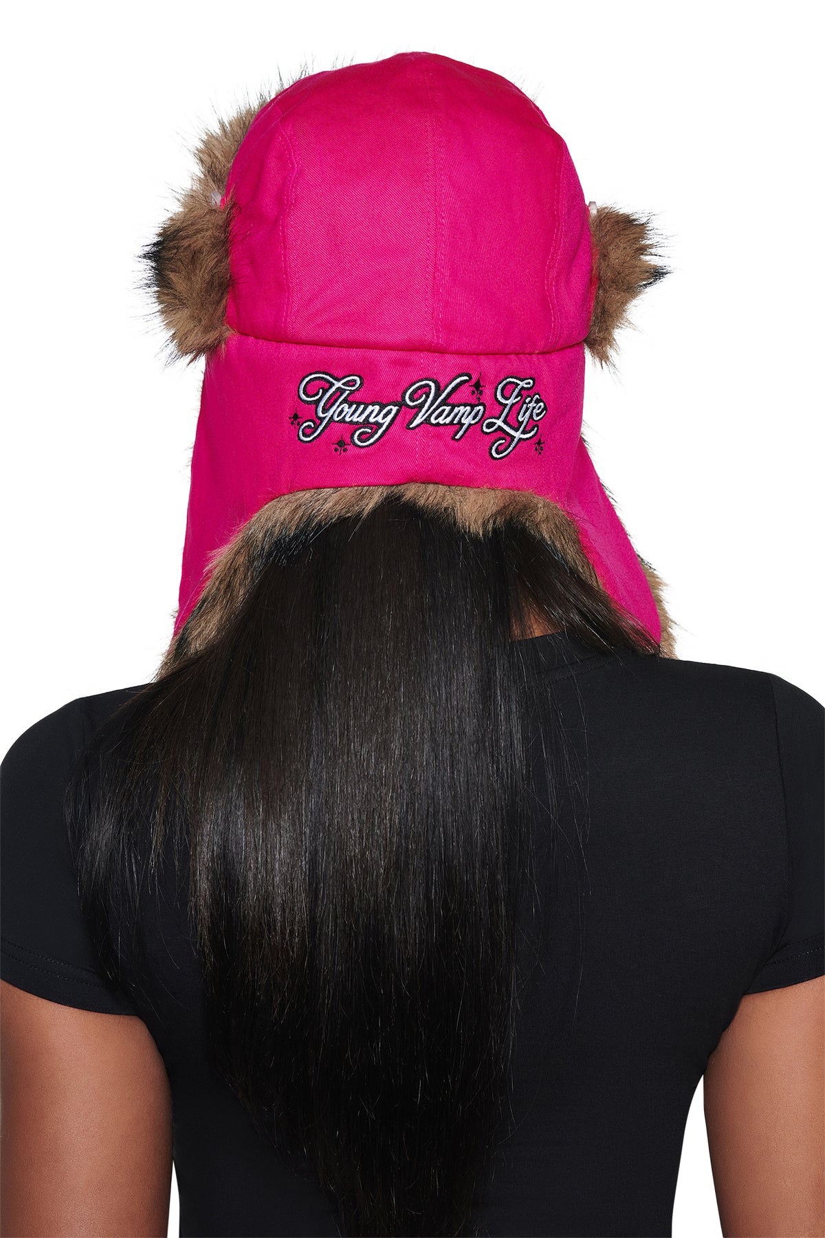 A person with long dark hair wears a bright pink I.AM.GIA YVL FUR TRAPPER HAT with brown trim and “Young Vamp Life” embroidered on the back.