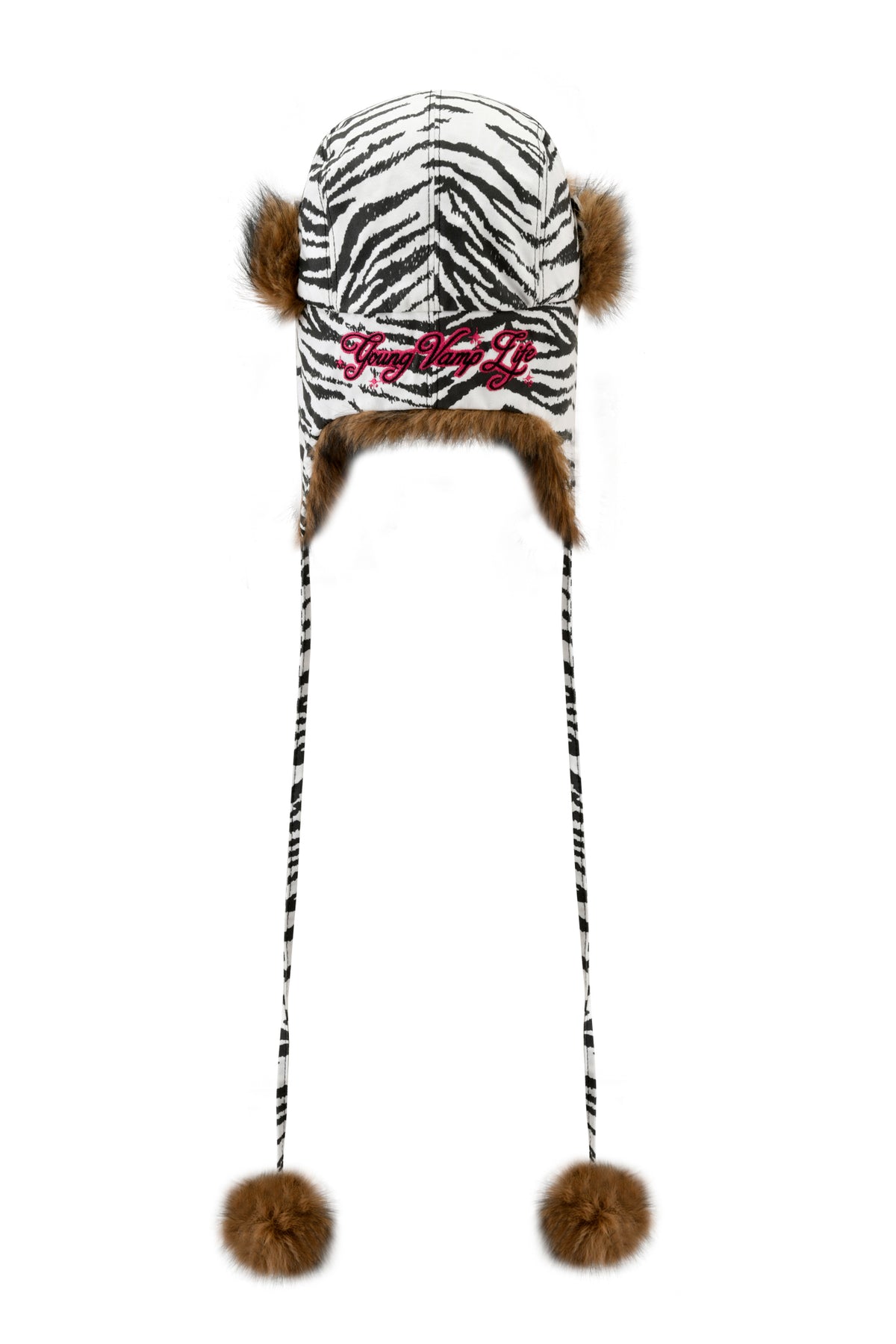 I.AM.GIA YVL FUR TRAPPER HAT - ZEBRA featuring zebra print, brown faux-fur lining, side pom-poms, long ties with pom-poms, and “Young Vamp Life” embroidered in pink on the front.