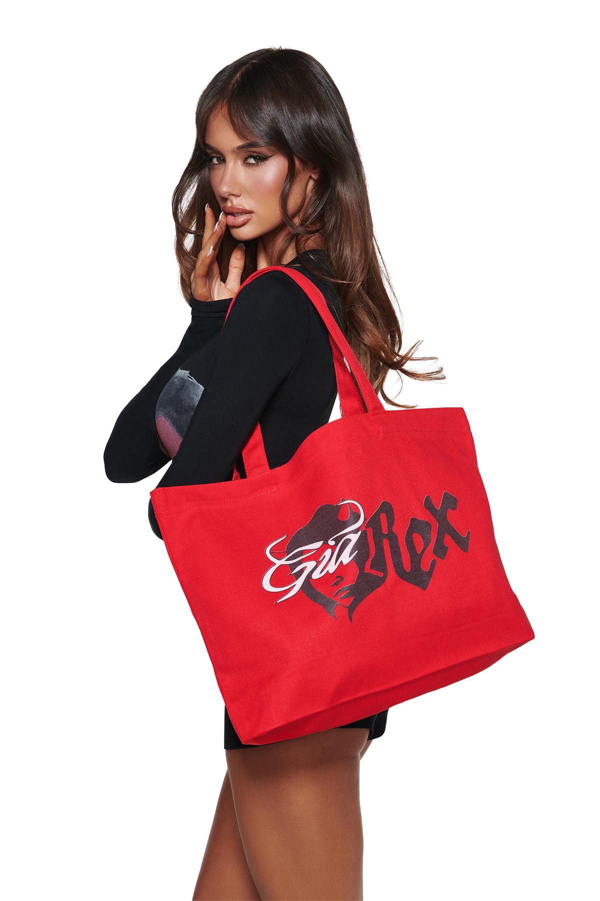 A woman in black poses with the T-REX TOTE BAG - RED by I.AM.GIA, featuring bold black and white graphics, a stylized face, and devil girl artwork against a plain white background.