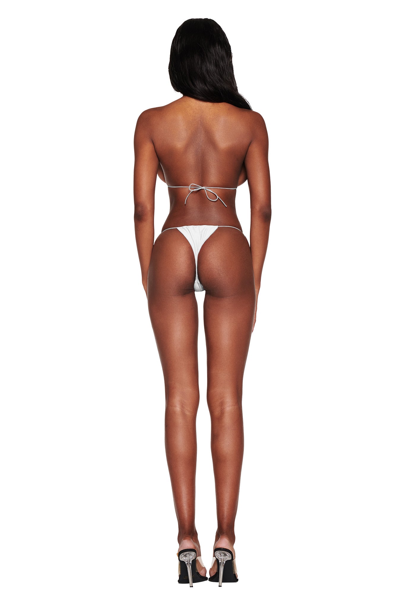 Rear view of a person with long hair wearing the I.AM.GIA Bambi Bikini Bottom in white and high heels, standing against a white background.