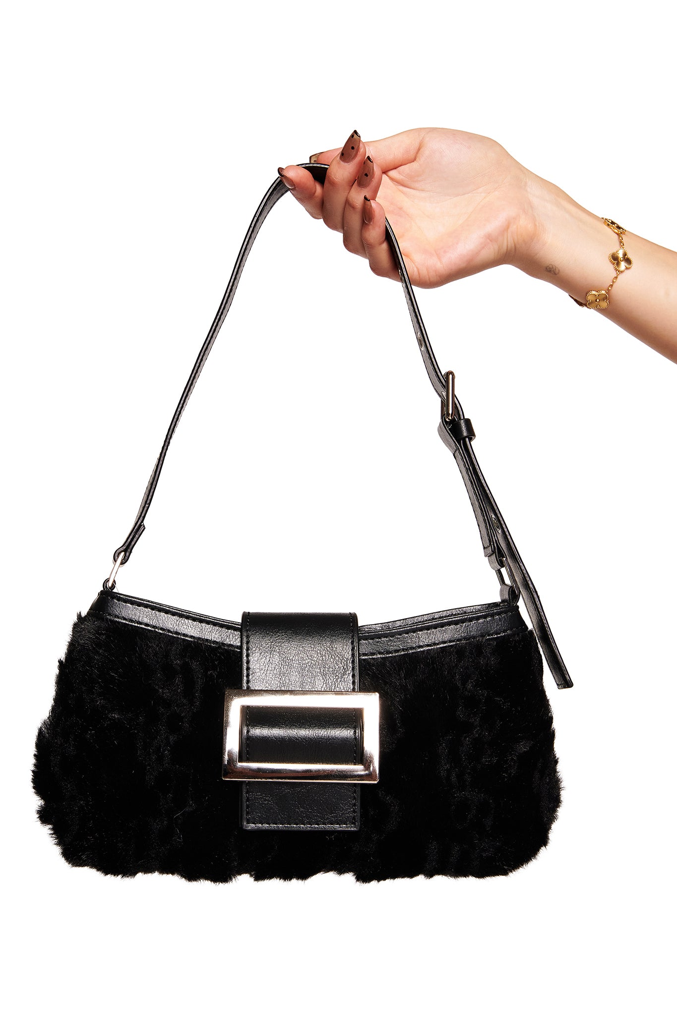 A hand with painted nails and a gold bracelet holds the I.AM.GIA RUBY PURSE - BLACK, a mini shoulder bag with faux fur and a rectangular silver buckle, against a white background.