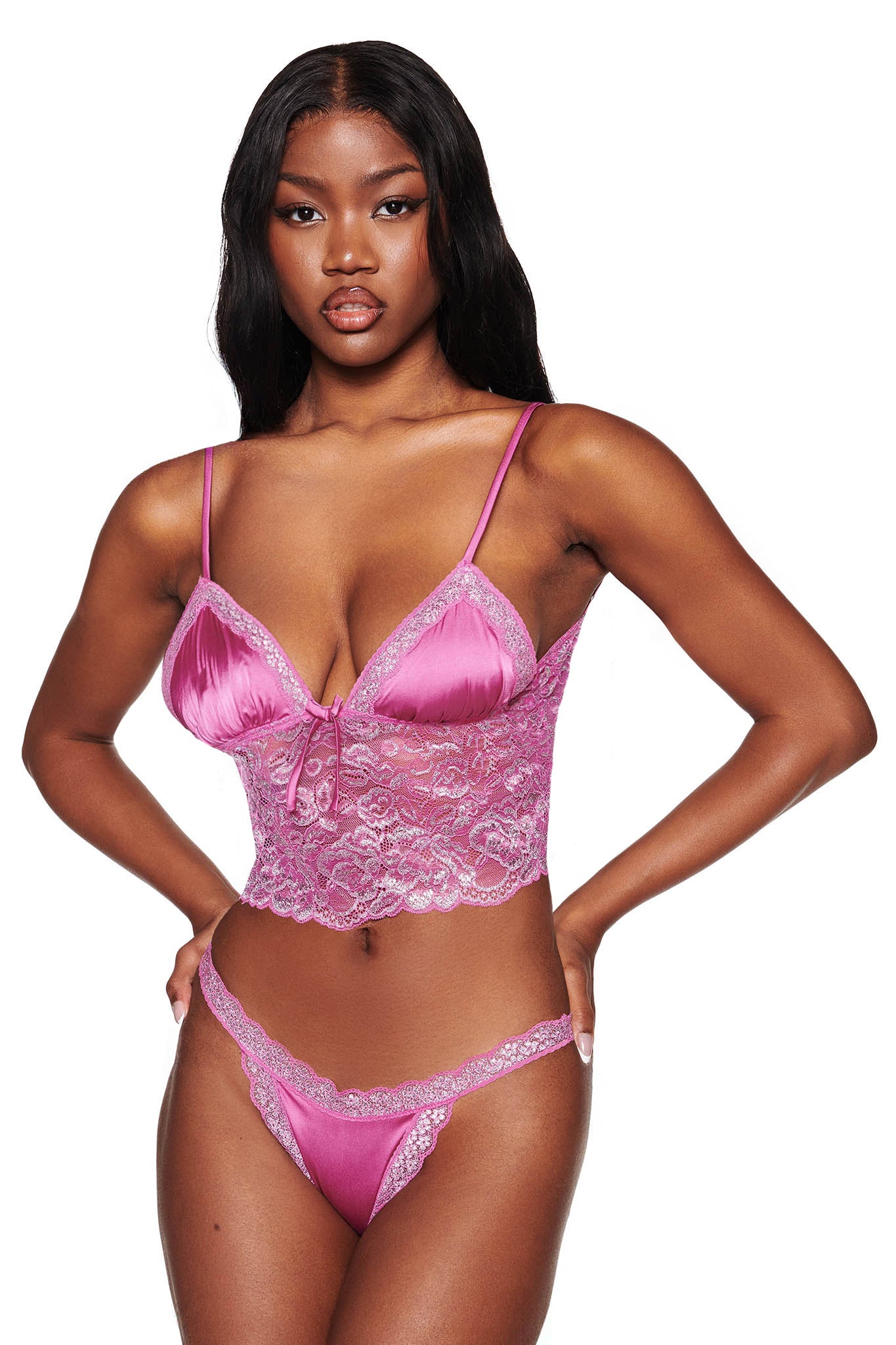 A woman confidently poses against a plain white background in the LOLO METALLIC SET - MAGENTA by I.AM.GIA. The set features a strappy satin top with adjustable shoulder straps, delicate lace details, and matching low rise thong bottoms.
