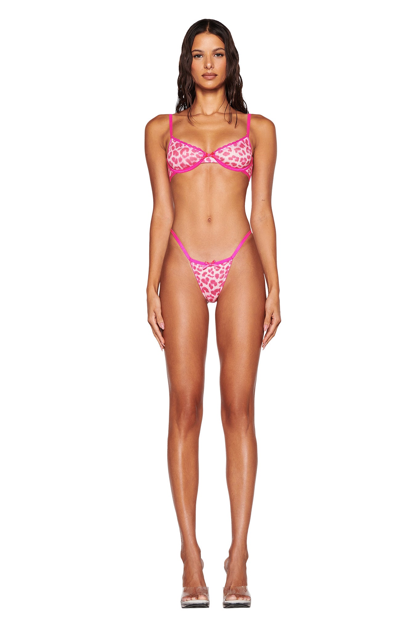 A woman exudes confidence in her I.AM.GIA SKYE SET 2.0 - PINK, presenting a striking pink leopard print design. Her long dark hair cascades down as she poses against a pristine white backdrop, complemented by clear high-heeled shoes.