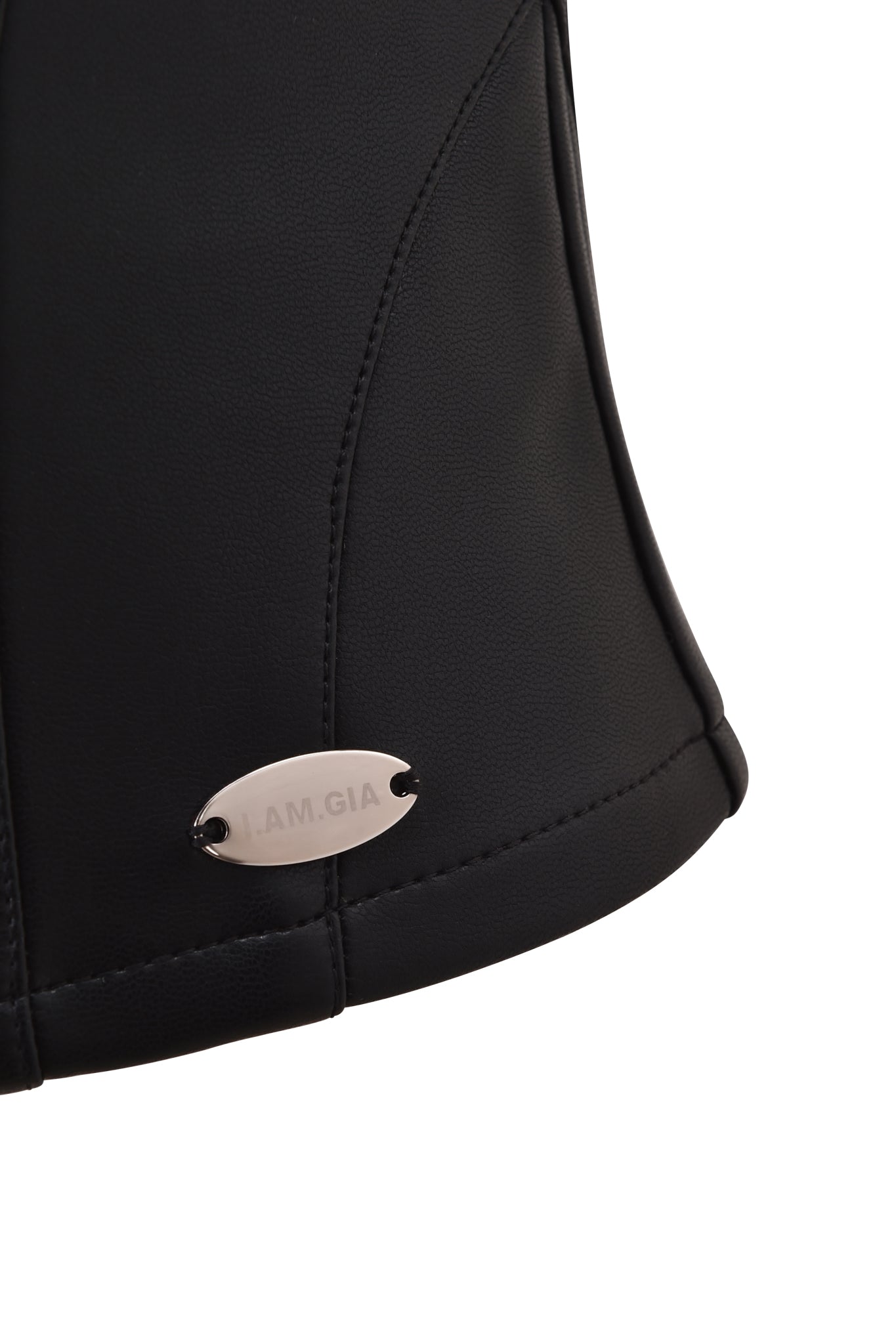 Close-up of the TEMPEST BUSTIER TOP by I.AM.GIA in black PU, showcasing curved stitching, a sweetheart neckline, and a small oval metallic tag engraved with "I.AM.GIA" near the hem.