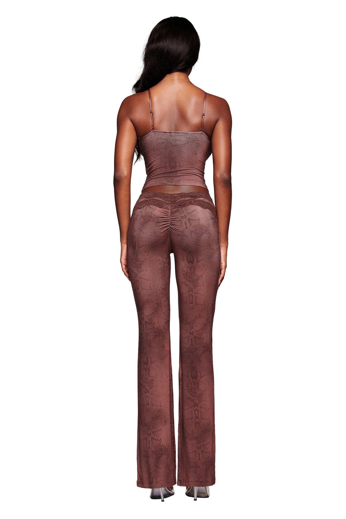 A woman with long dark hair faces away, wearing the I.AM.GIA BEAU TOP in brown and matching flared pants with a subtle pattern, paired with high-heeled shoes, all set against a white background.