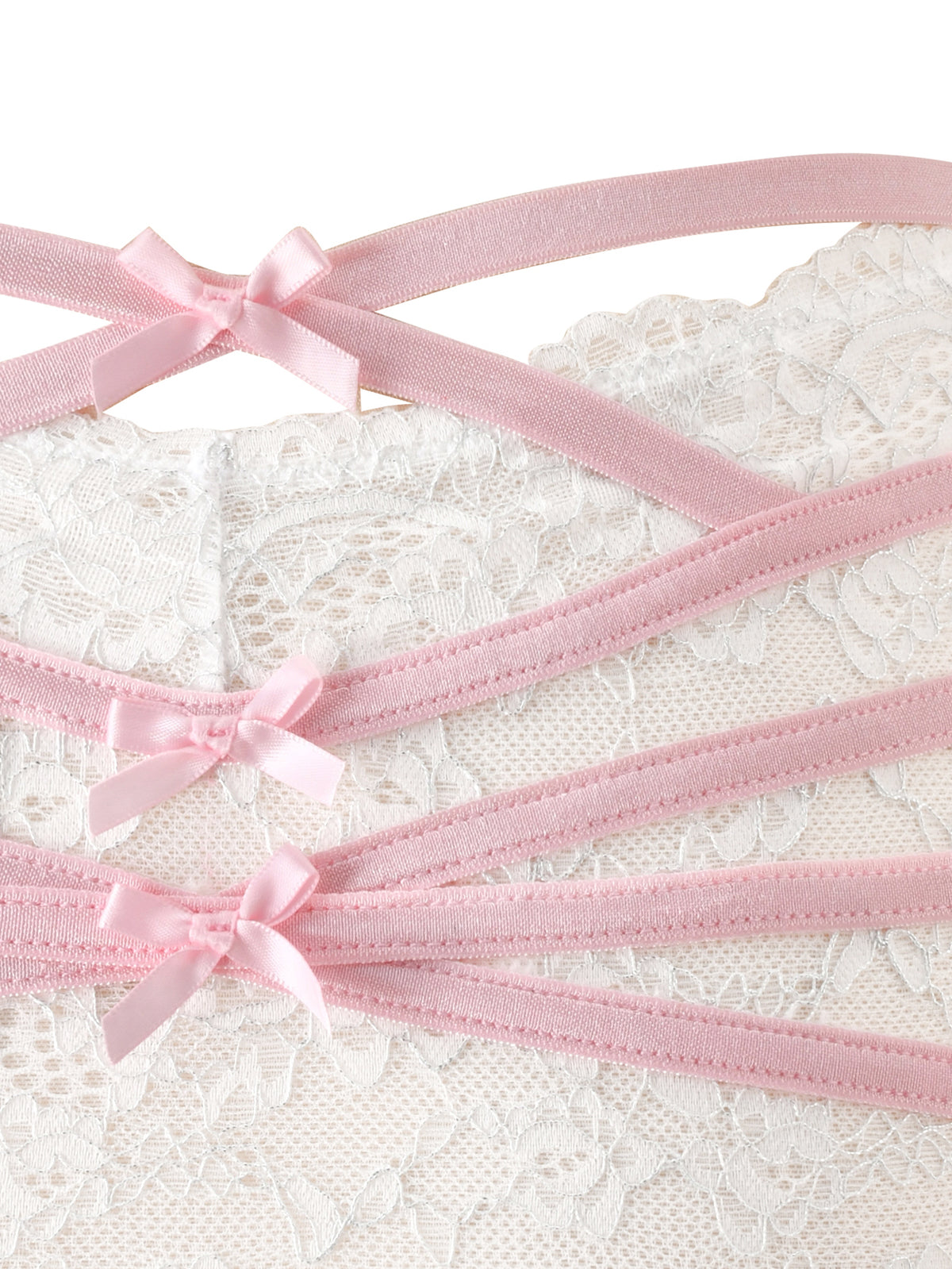 A close-up of the BUNNY LINGERIE SET - WHITE PINK by I.AM.GIA showcases three pink satin straps, each accented with a small pink ribbon bow, set diagonally across soft white lace fabric—capturing the delicate charm of vintage-inspired lingerie.