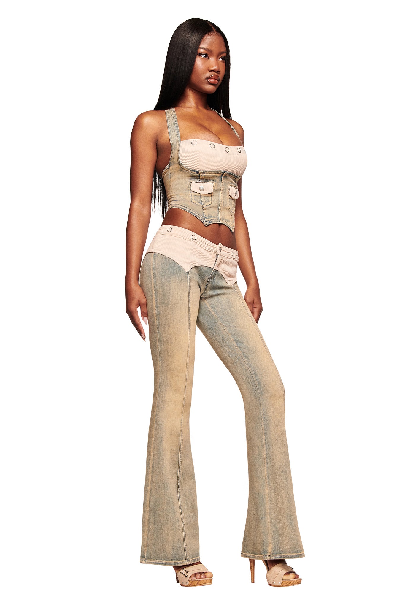 A woman wears the I.AM.GIA TOMMIE CORSET in antique denim— a structured, button-up crop top with pocket details—paired with matching flared jeans, high-heeled sandals, and her long, straight hair styled sleekly.