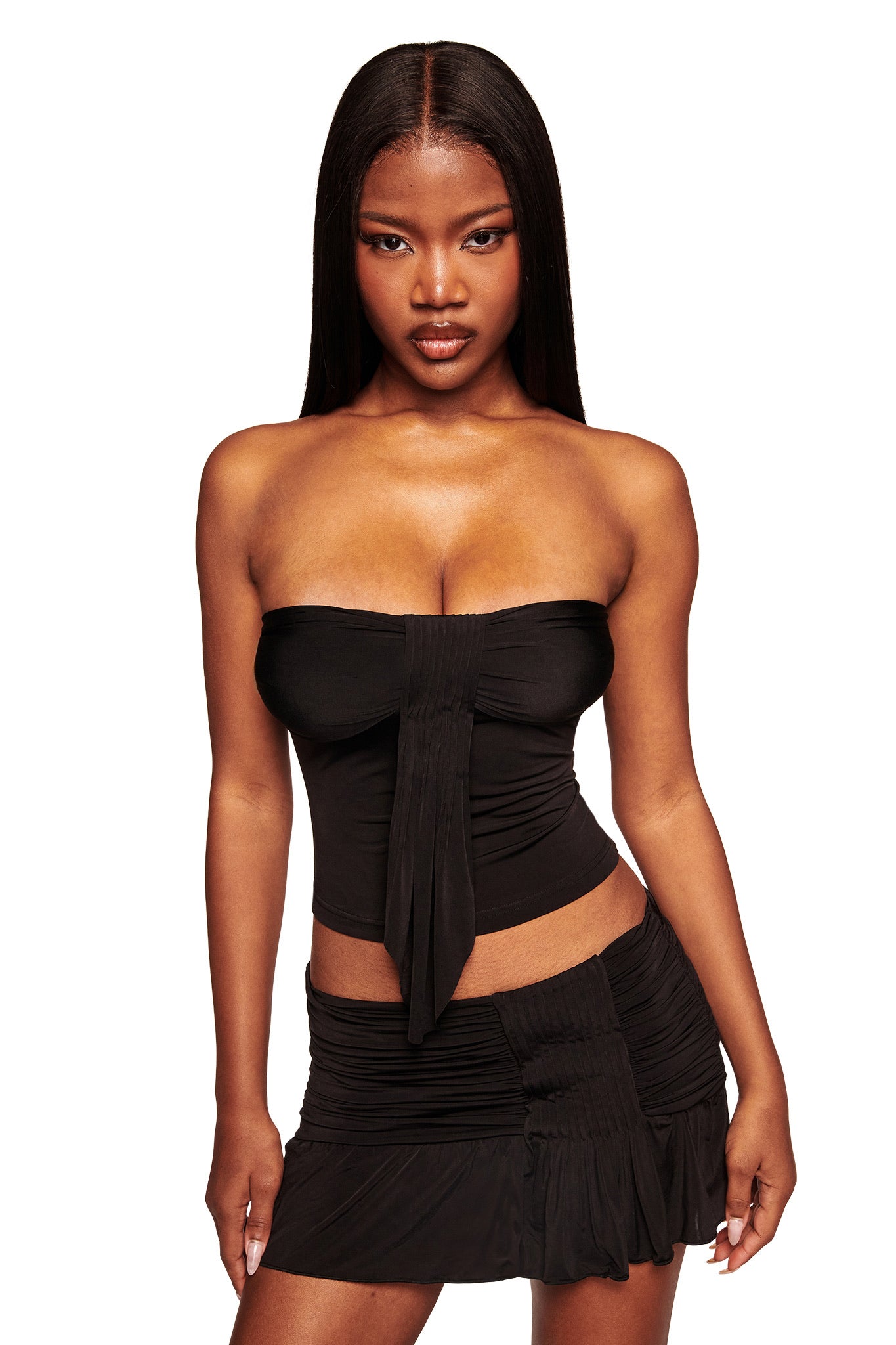 A woman with long straight hair wears the I.AM.GIA ELYSIA MINI SKIRT in black and a matching strapless front-tie top, standing facing forward against a white background.