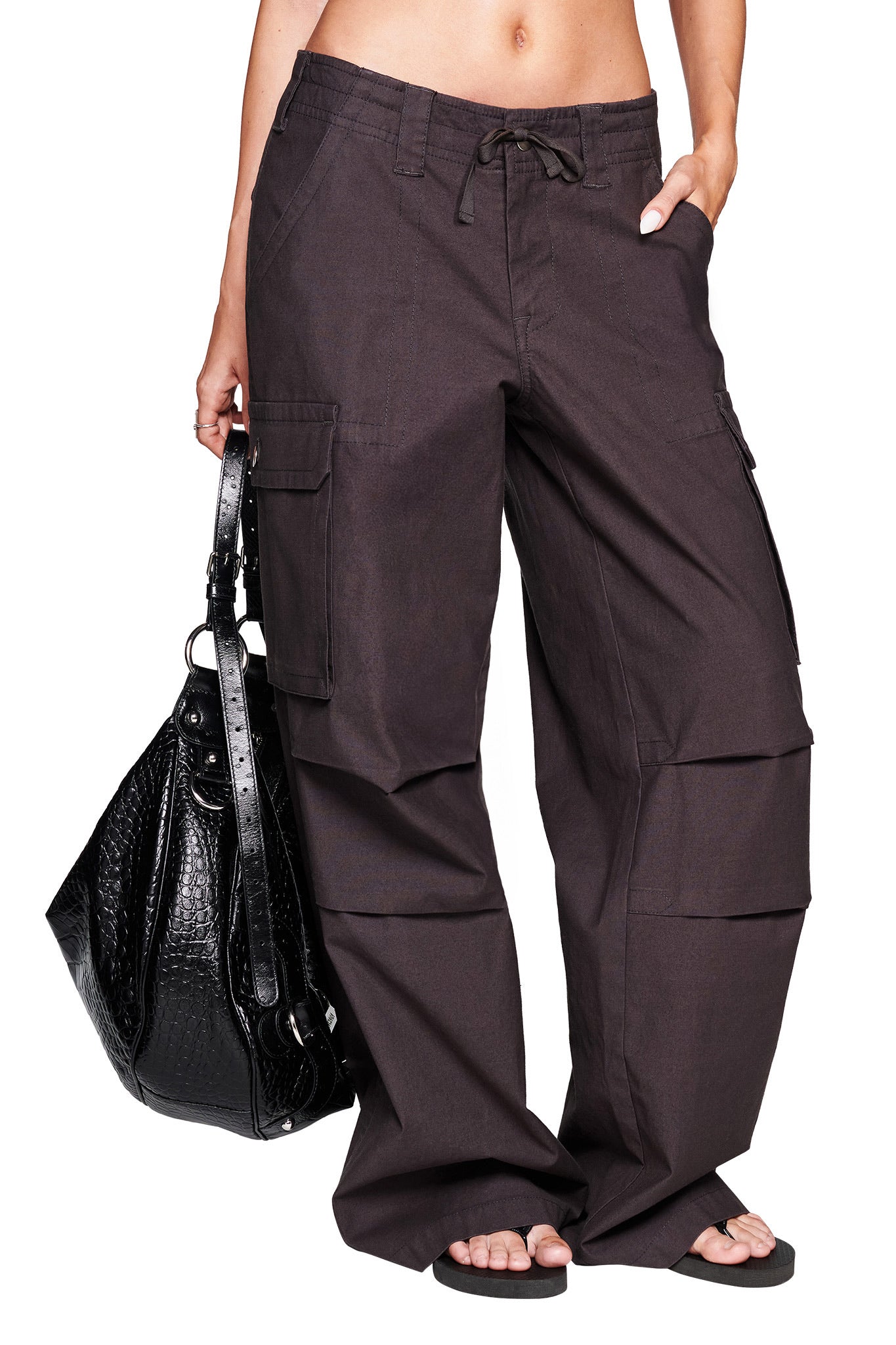 A person wearing I.AM.GIA JAXXON PANT in grey with an oversized fit and large side pockets, holding a black textured handbag, and wearing black sandals. The person's midriff is visible.