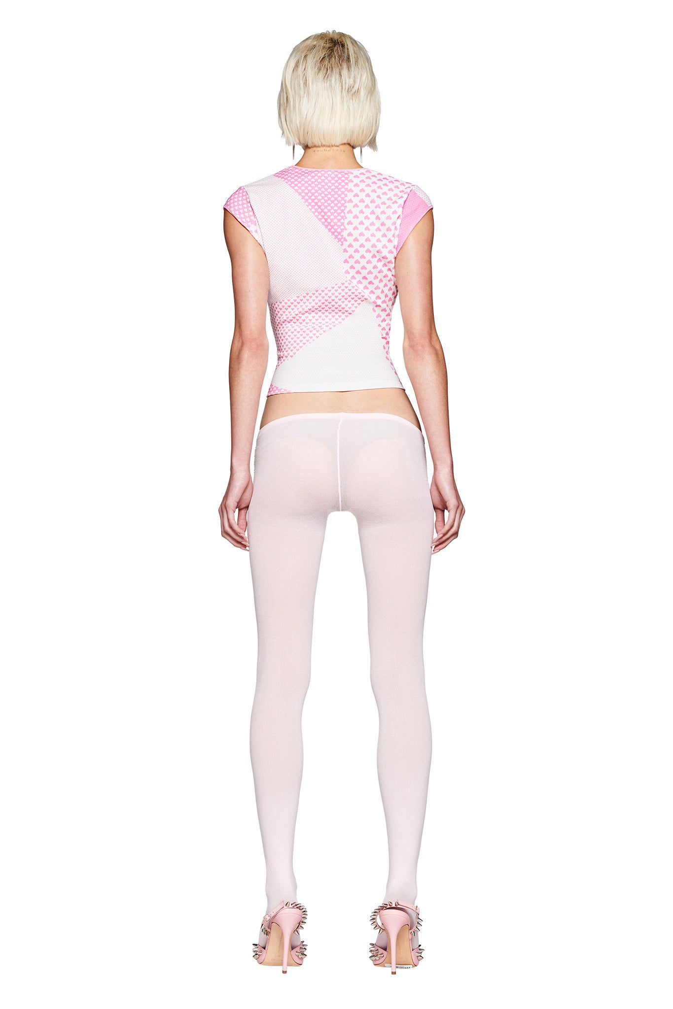 A person with short blond hair faces away against a white background, wearing the I.AM.GIA FAFI TOP in pink with diamanté details, sheer white tights, and pink ruffled high-heeled sandals.