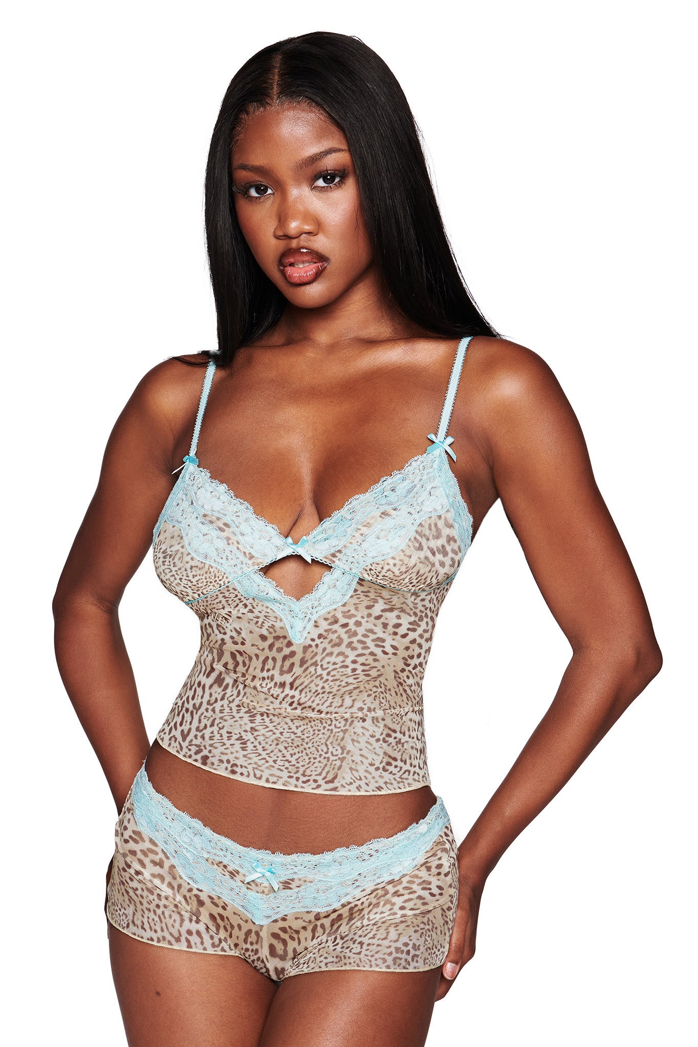 A woman wears the I.AM.GIA TASHA SHORT - LEOPARD LIMBO set, featuring leopard print hot shorts and a matching camisole with aqua blue lace trim. She stands against a white background with long, straight hair.