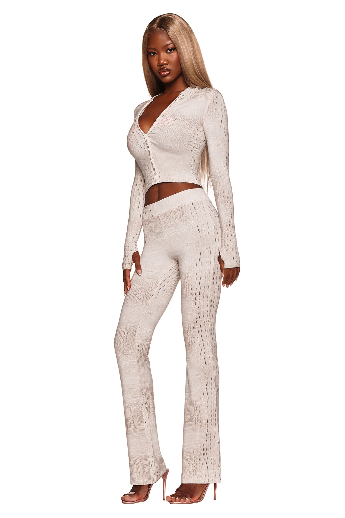 A woman with long straight hair wears a fitted beige knit top and the I.AM.GIA BLARE TRACKPANT - HOT CROC, paired with heeled sandals, standing against a white background.
