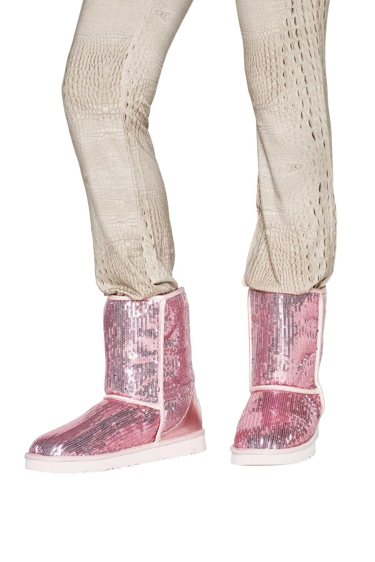 A person wearing textured beige pants and the I.AM.GIA ELVIRA SEQUIN BOOT in pink stands against a white background.