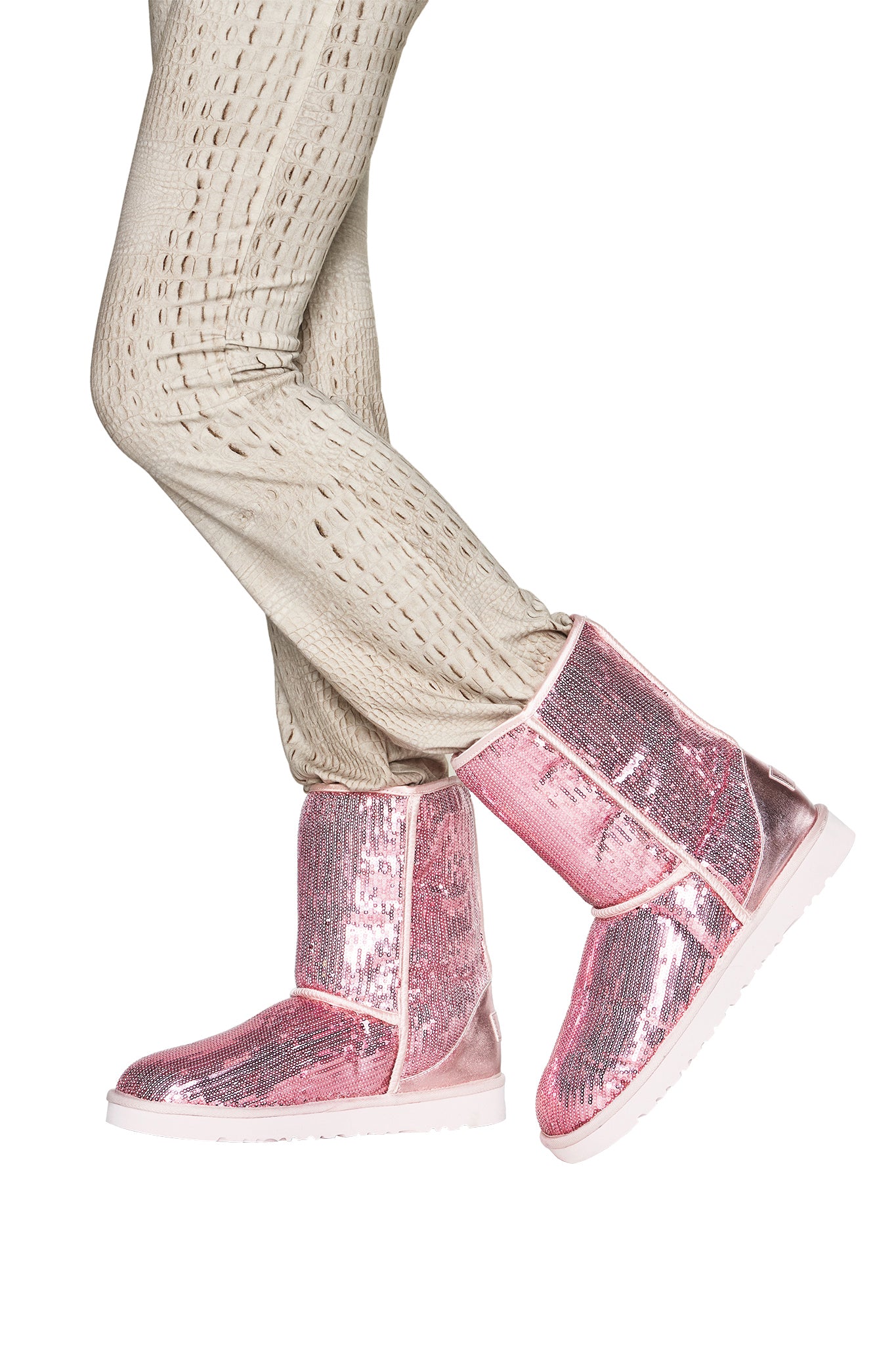 A person wearing beige textured pants and the I.AM.GIA ELVIRA SEQUIN BOOT in pink, shown from the hips down against a white background.