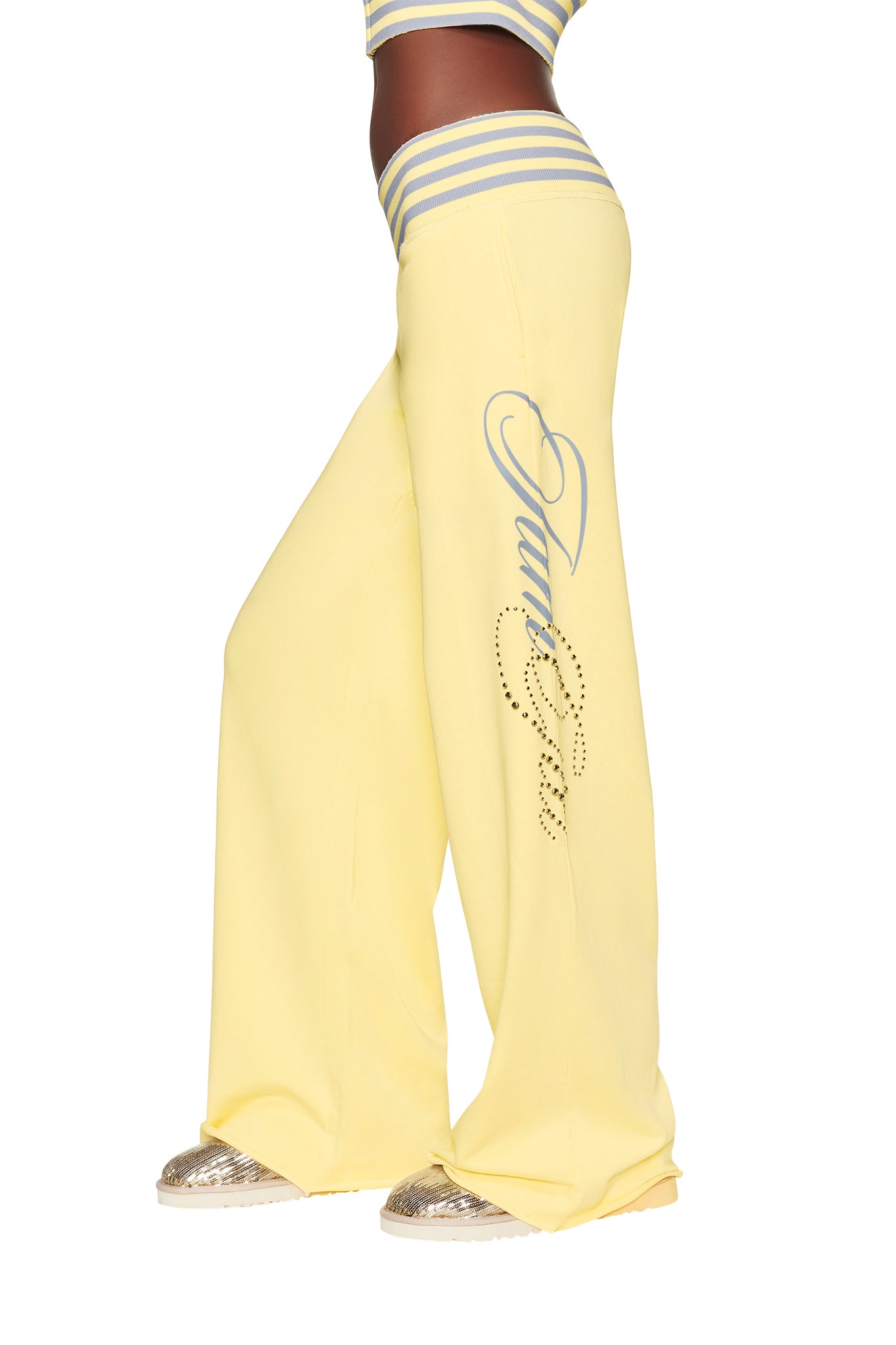 A person wearing the I.AM.GIA VEDA PANT - YELLOW, which features wide legs and embellished rhinestone detailing, styled with a striped crop top and metallic sneakers.