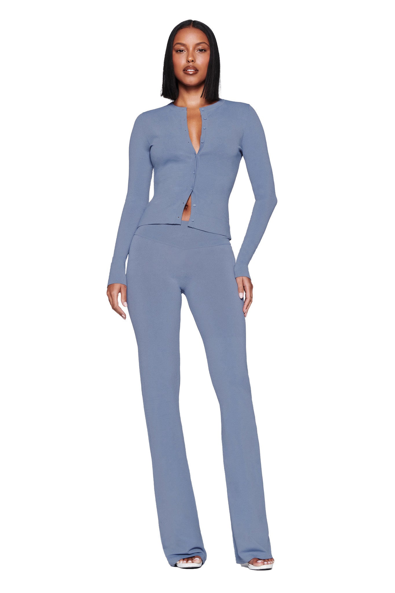 Against a white background, a person stands confidently wearing the I.AM.GIA AUDRINA PANT in steel blue, featuring buttons down the front and a bodycon fit. Their straight, shoulder-length hair complements the sleek look.
