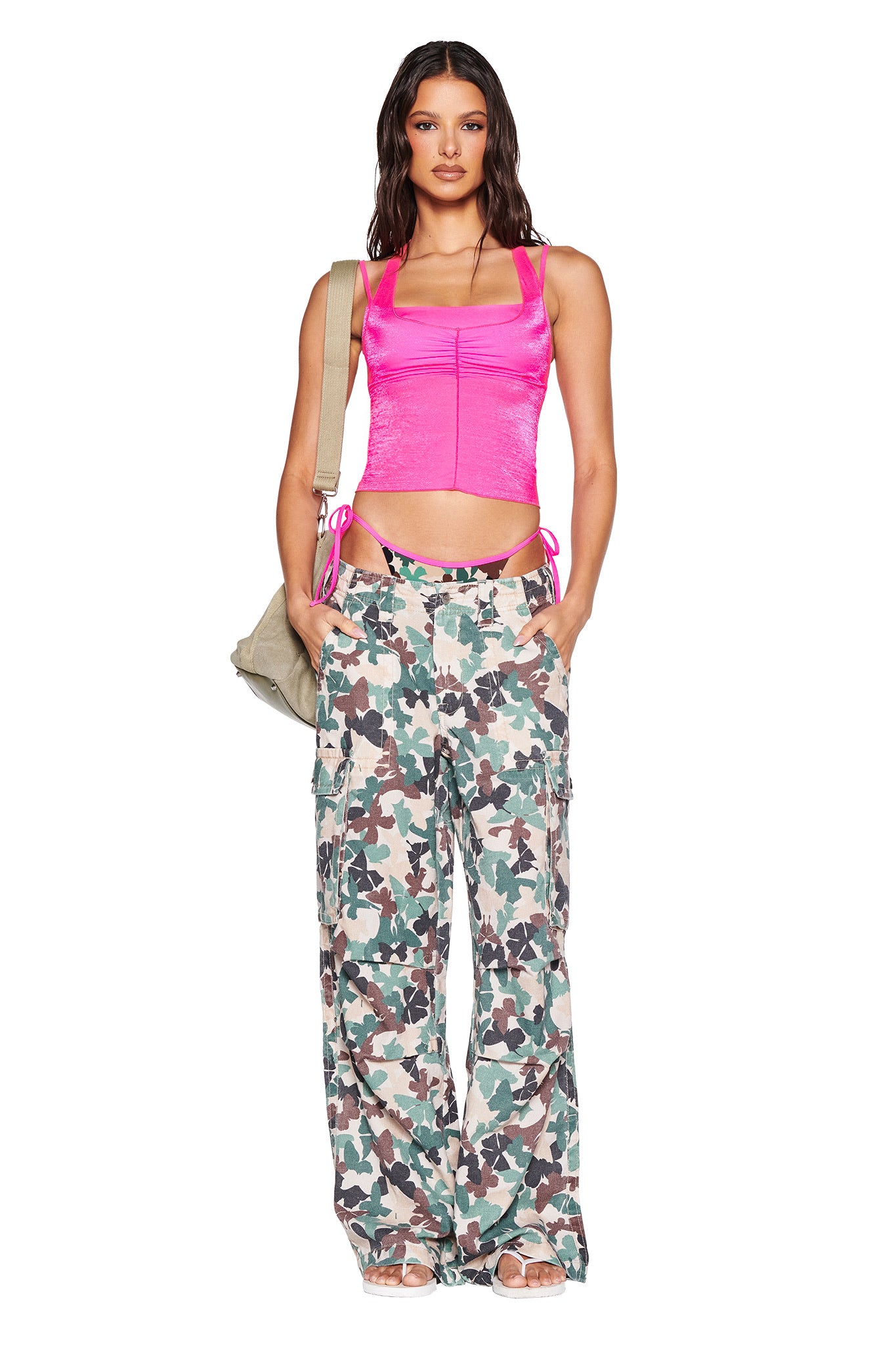 A woman stands out in an I.AM.GIA bright pink crop top and EFFIE CARGO PANT - FLUTTER CAMO. She effortlessly carries a beige bag over her shoulder, adding a casual touch to her vibrant look.