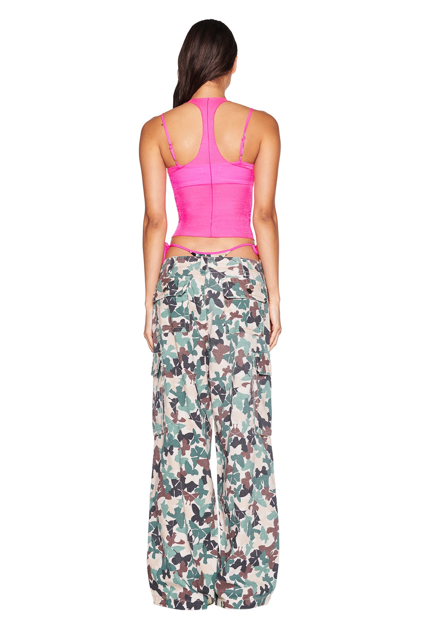A person with long dark hair, wearing the I.AM.GIA NERINA TOP in neon pink and loose camouflage cargo pants, stands against a white background, with the bodycon fit accentuating their silhouette.