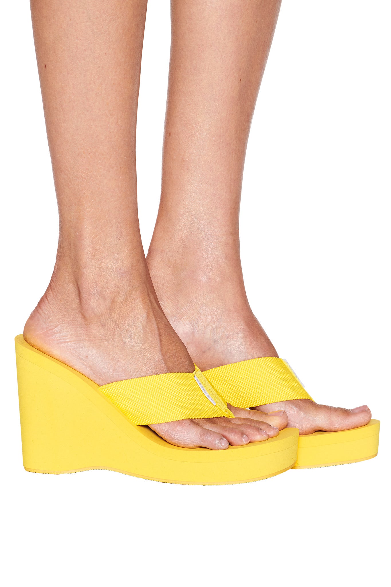 A person models the I.AM.GIA SHELBY FLIP FLOP - YELLOW sandals, displaying bare feet and lower legs against a white background.