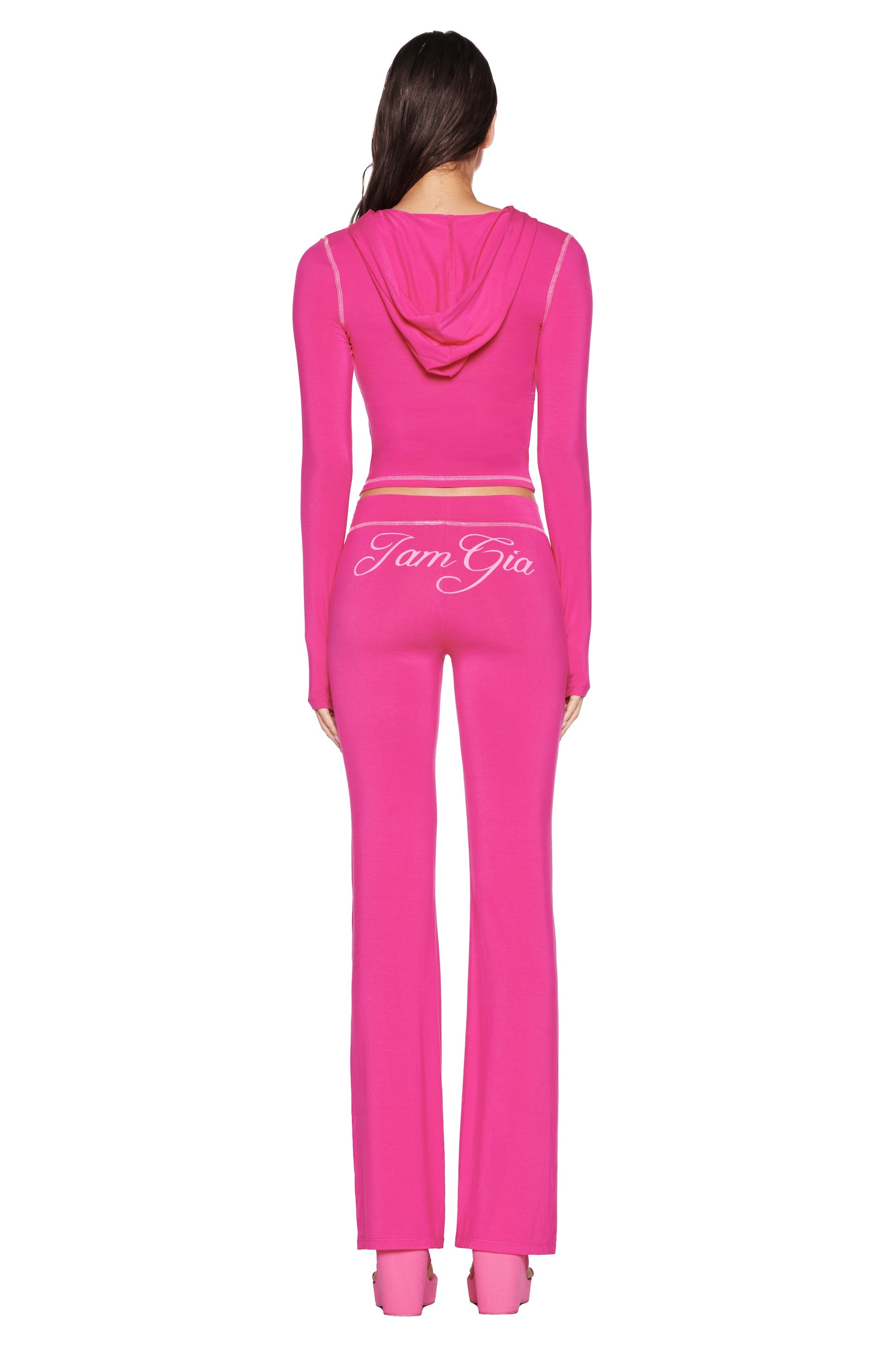 A person in the BLARE TRACKPANT - HOT PINK by I.AM.GIA stands facing away from the camera, showcasing the logo across the lower back against a white backdrop.