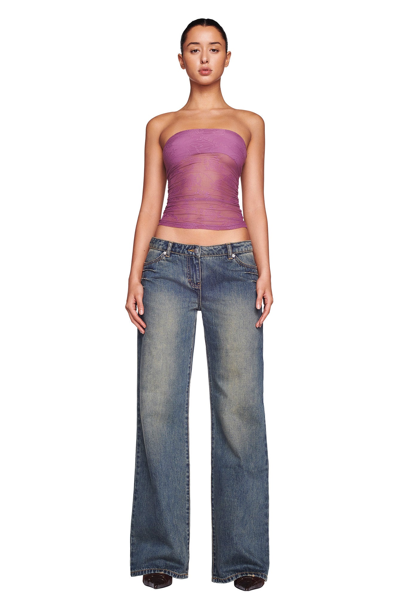 A person stands facing forward against a white background, wearing a strapless, sheer purple tube top and the DYLAN JEAN in blue denim from I.AM.GIA. Their hair is pulled back, and they are wearing dark shoes. With a confident stance and arms relaxed by their sides, they exude effortless style.