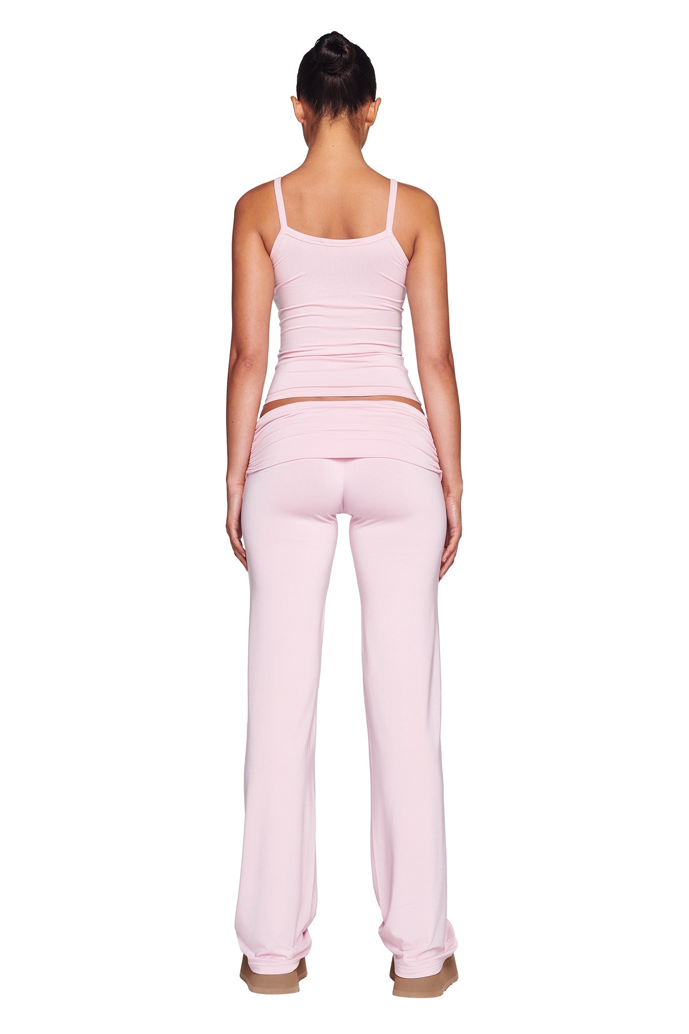 A person with long hair tied up, standing with their back to the camera. They are wearing the cozy ERIN TOP in pink and low-rise pink pants made from bamboo fabrication by I.AM.GIA, along with beige shoes. The outfit is casual, matching, and designed for comfort with a bodycon silhouette.