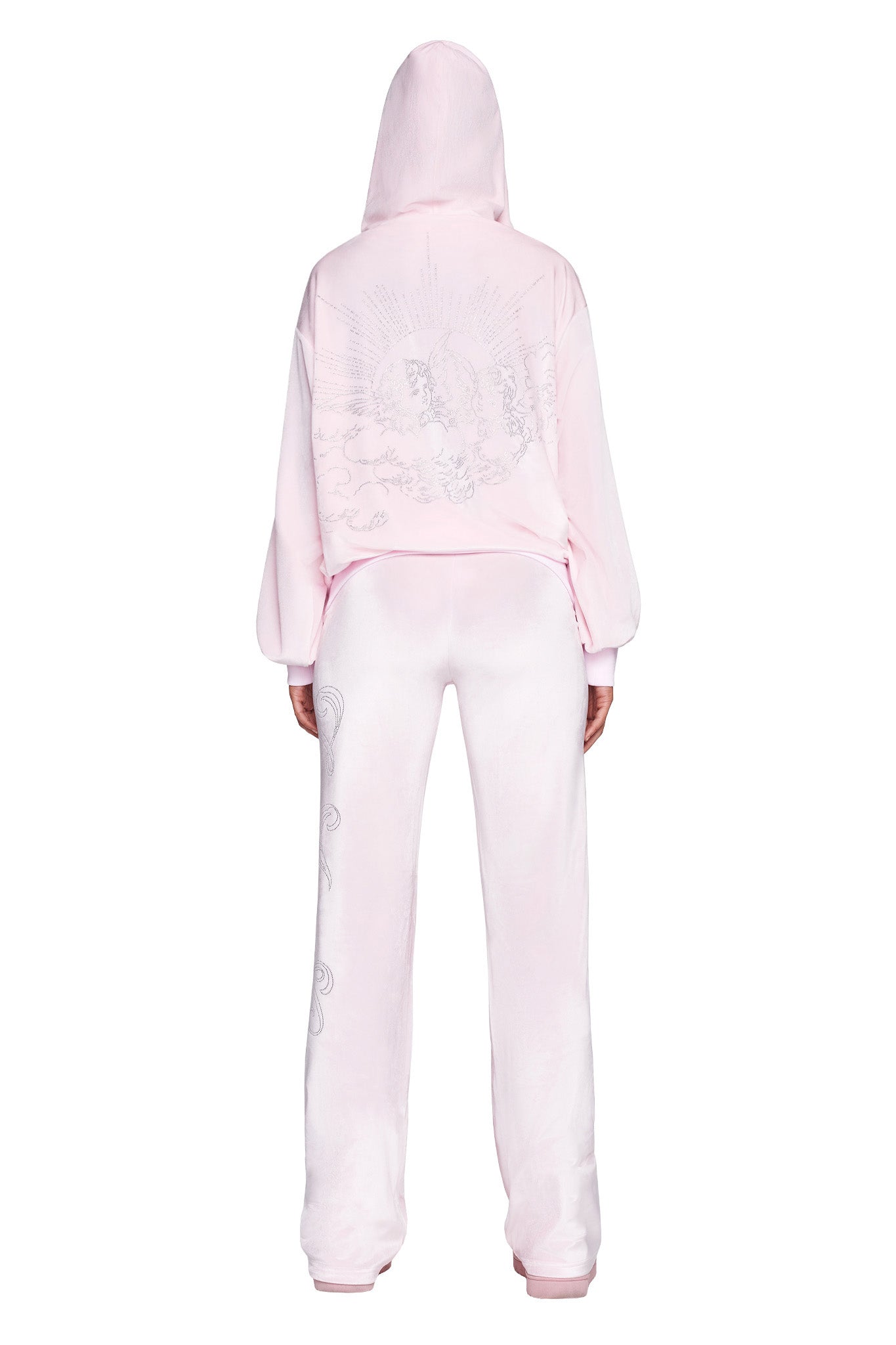 A person is standing with their back to the camera, wearing an icy pink DARIA HOODIE by I.AM.GIA and matching light pink pants. The hoodie features a large, intricate design on the back, while the pants have small decorative patterns on the sides.