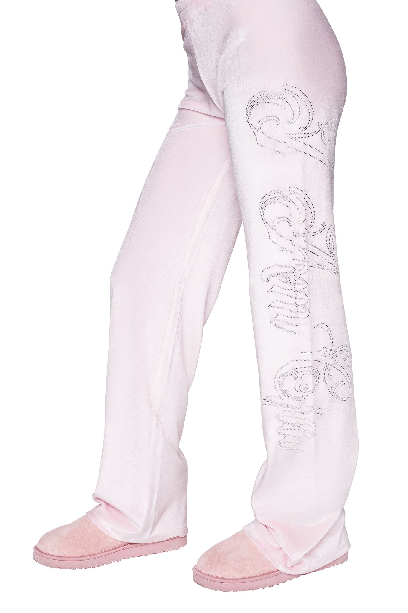 The image shows a person standing in I.AM.GIA's DARIA PANT - PINK : ICY PINK, featuring a custom 'I.Am.GIA' logo along the side of the left leg. The person is also wearing soft pink slippers. The upper part of the body is not visible.