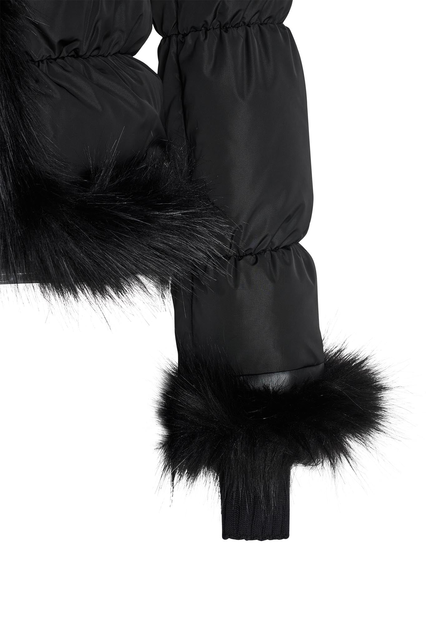 Close-up of a black BILLIE JACKET by I.AM.GIA with faux-fur trim. The image focuses on the bottom edge of the sleeve and part of the body, showcasing the fur lining and elastic cuff detail. The jacket material appears thick and insulated.