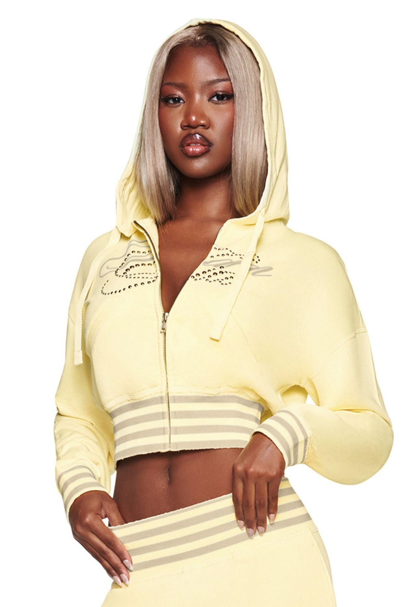 A woman with straight blonde hair stands confidently against a white background, wearing the I.AM.GIA VEDA JACKET in yellow, which features a zip-up front and striped cuffs and hem.
