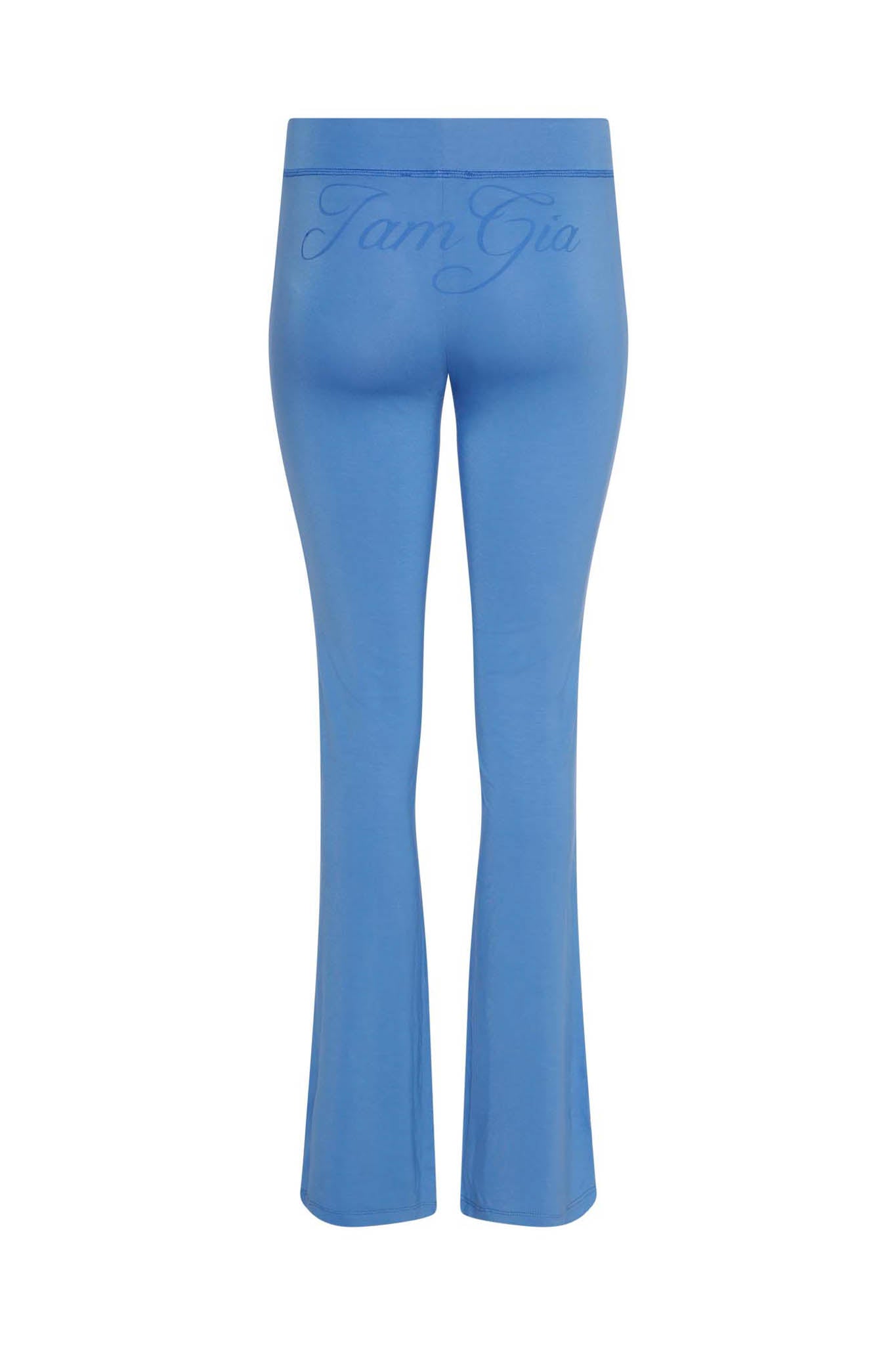 A rear perspective of the BLARE TRACKPANT - BLUE from I.AM.GIA highlights its high-waisted, flared legs and bodycon silhouette. The "I.AM.GIA" logo is embroidered at the top of the waistband, and the fabric looks smooth with a slight stretch.